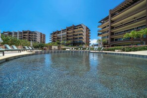 Une piscine aux eaux cristallines, dotée de chaises longues, et un bâtiment avec de nombreux balcons en arrière-plan.