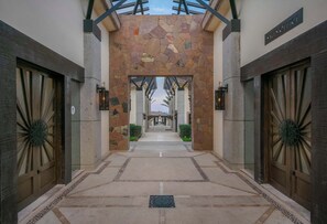 Un pasillo con paredes de piedra y puertas de madera, que conduce a un espacio cubierto con vista al cielo.