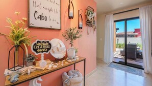 A room with a pink wall, a welcome sign, a table with seashells, and a view of the outside.