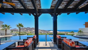 A poolside area with wicker furniture and a view of the ocean.