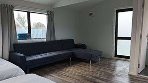 Une pièce avec un canapé de couleur sombre, un lit avec une literie blanche et un plancher en bois.