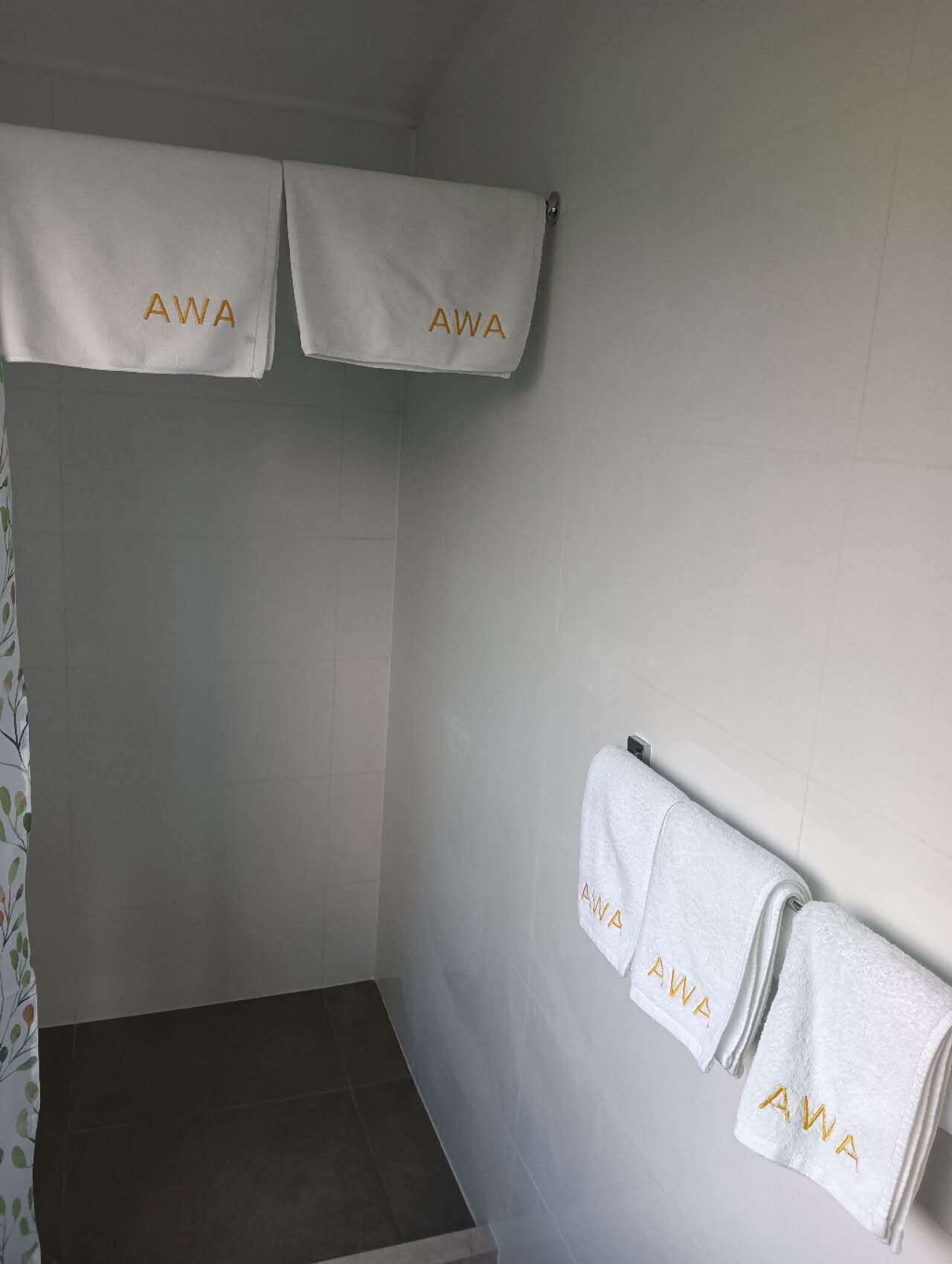 Ein Badezimmer mit zwei Handtüchern an einem Halter, jedes mit 'AWA' in Gold bestickt.