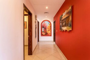 Un pasillo con pared roja, suelo de baldosas y un cuadro de una escena callejera.