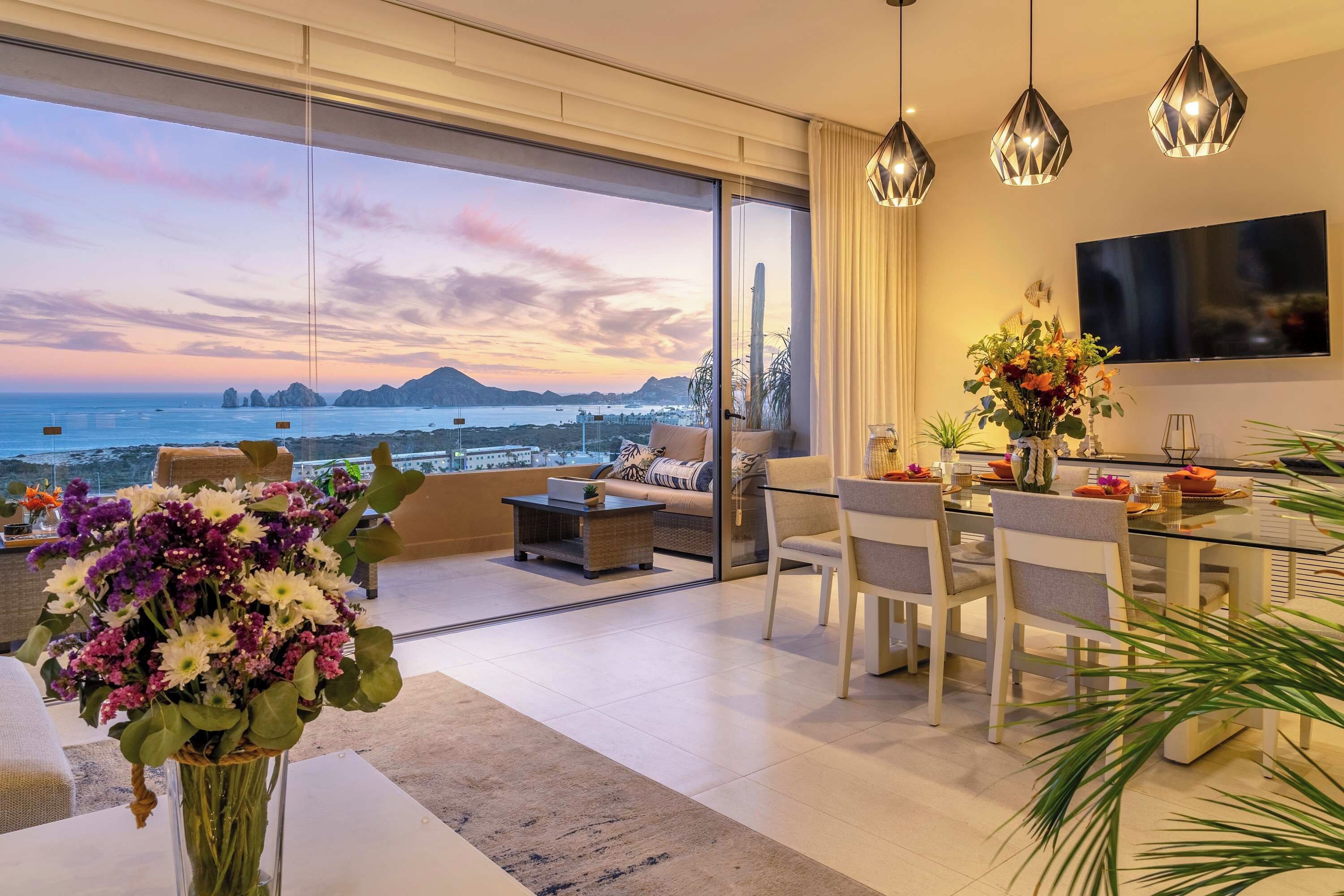 A modern living room with a large glass door leading to a balcony overlooking a scenic view of the sea and mountains.