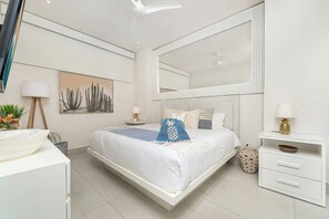 A modern bedroom with a large bed, a bedside table, a mirror, and a wall-mounted artwork.