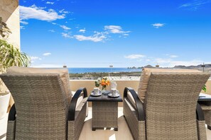 A balcony with wicker chairs, a table, and a view of the sea.