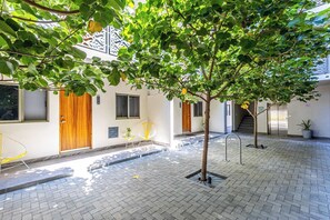 A courtyard with a tree, a yellow chair, a wooden door, and a staircase.
