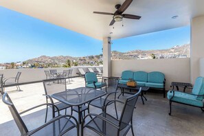 A rooftop terrace with outdoor seating, a ceiling fan, and a view of distant hills.