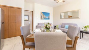 A modern living room with a dining table, two sofas, a ceiling fan, and a large window. - Centric Apt in Downtown - Rooftop Pool - Terrace (Cabo San Lucas)