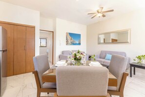 A modern living room with a dining table, two sofas, a ceiling fan, and a large window.