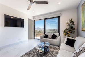 A modern living room with a large window, a ceiling fan, and a flat-screen TV.