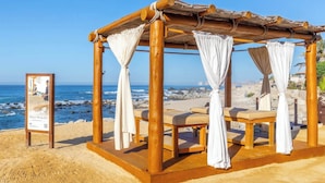 A beachside gazebo with four cushioned benches, a wooden structure, and a view of the ocean.