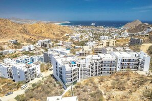 A coastal residential area with modern buildings, a clear view of the sea, and a hilly landscape in the background.