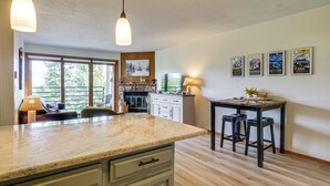 Una cocina con encimera de mármol, armarios de madera, zona de comedor con mesa y taburetes, y chimenea.