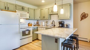Una cocina con alacenas verde claro, un refrigerador blanco, microondas, horno, lavavajillas e isla de mármol con dos taburetes.