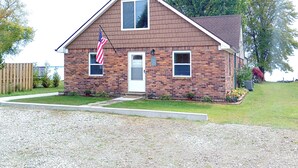 A two-story brick house with a front porch, a small front yard, and an American flag.