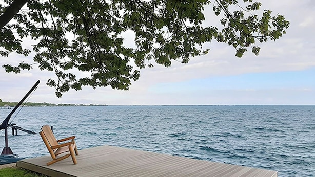 A wooden deck with a single wooden chair, overlooking a body of water.