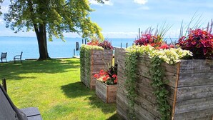 A grassy area with wooden planters containing flowers and plants, a bench, and a view of the water.