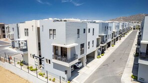 A row of modern, multi-story residential buildings with balconies, a clear sky, and a mountain in the background. - Chic 2BR House - Tezal - Private Rooftop - Pool (Cabo San Lucas)