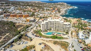 An aerial view of a coastal resort with multiple buildings, a swimming pool, and a beach.