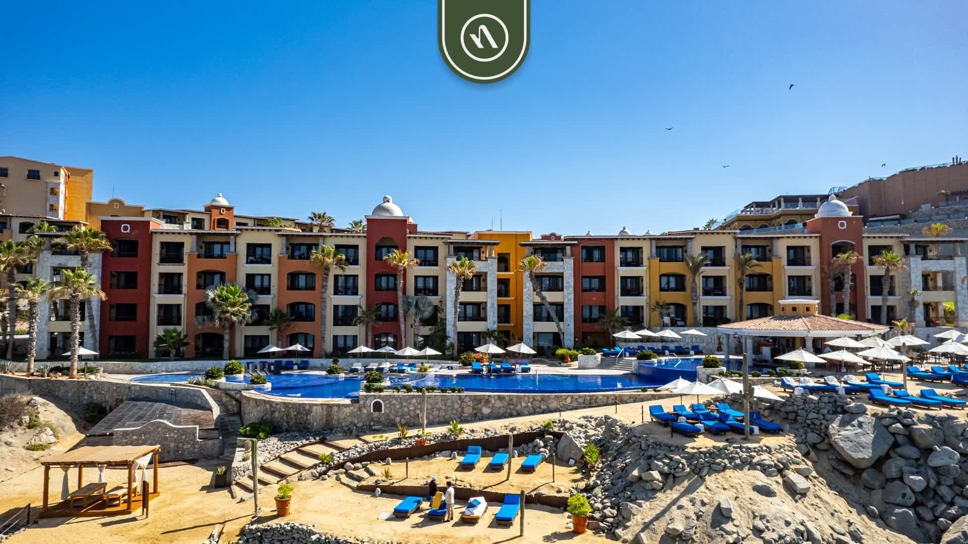 A hotel with colorful buildings, a swimming pool, and lounge areas with umbrellas.