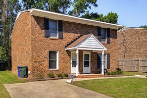 A two-story brick house with a front porch, a garage door, and a wooden fence.