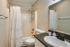A bathroom with a shower, toilet, sink, and a mirror.