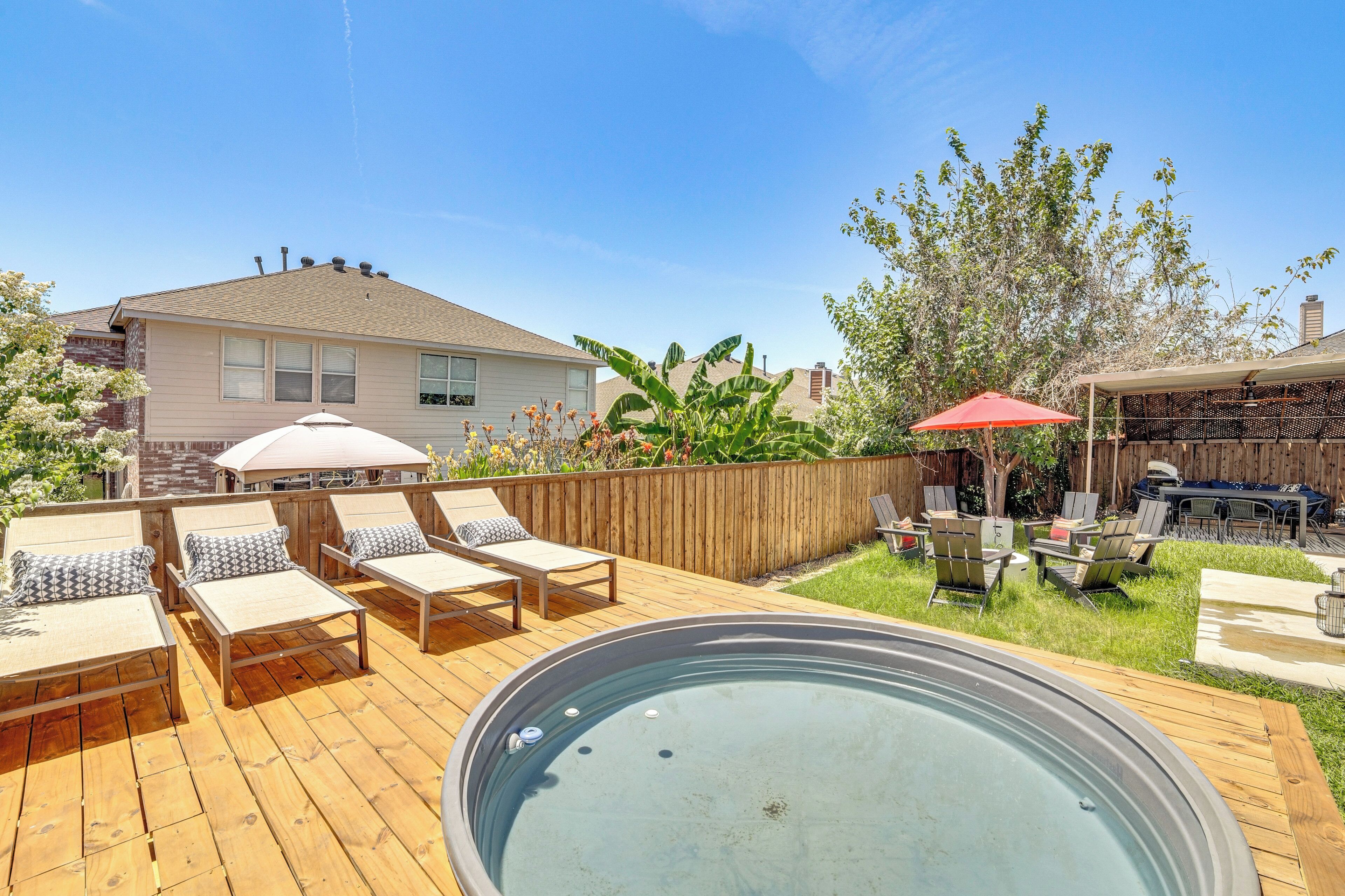 Un patio trasero con una terraza de madera, un jacuzzi, sillas de descanso y una zona de barbacoa.