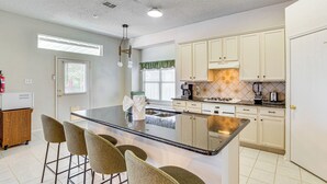 A kitchen with a central island, bar stools, and white cabinets. - Group-Friendly Grand Prairie Home w/ Perks! (Grand Prairie)