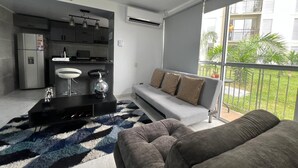 Ein modernes Wohnzimmer mit einem grauen Sofa, einem schwarzen Couchtisch und einem Essbereich mit einem weißen Tisch und Stühlen.