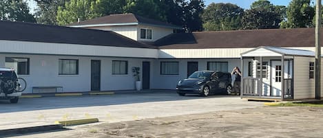 A motel with a parking lot, a covered outdoor seating area, and a building with a brown roof.