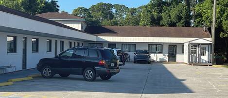 A parking lot with several cars, a small building with a porch, and trees in the background.