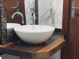 Un baño con un lavabo blanco, un tocador de madera, un espejo con diseño floral y un perchero para toallas.