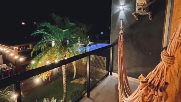 A balcony with a hammock, a palm tree, and string lights. - Pousada Rosa Paradise (Imbituba)