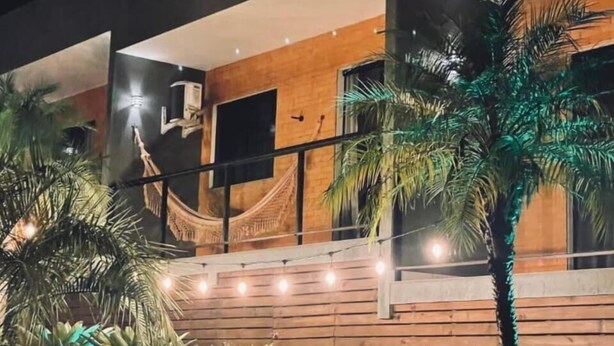 A modern building with a wooden facade, a hammock, and string lights. - Pousada Rosa Paradise (Imbituba)