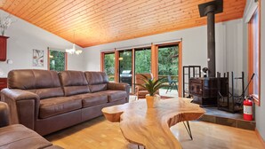 A modern living room with a brown leather sofa, a wooden coffee table, and a wood-burning stove. - Cozy 3BR Lakefront Retreat Featuring Sauna, Hot Tub, Kayaks (Ditch Lake)