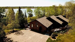 A cabin with a gravel driveway, surrounded by trees and a lake. - Cozy 3BR Lakefront Retreat Featuring Sauna, Hot Tub, Kayaks (Ditch Lake)