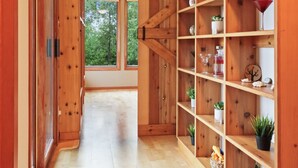 A hallway with wooden flooring and shelves on the right, leading to a window with a view of trees. - Cozy 3BR Lakefront Retreat Featuring Sauna, Hot Tub, Kayaks (Ditch Lake)