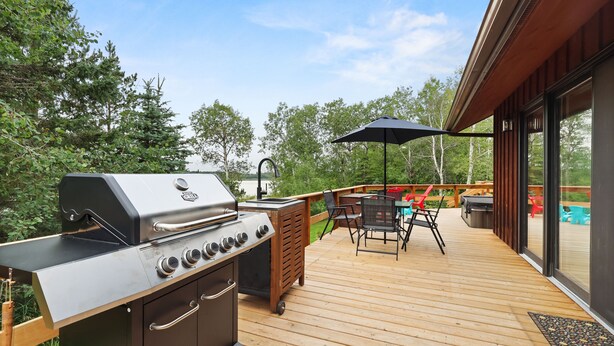 A deck with a grill, outdoor furniture, and a view of the surrounding forest. - Cozy 3BR Lakefront Retreat Featuring Sauna, Hot Tub, Kayaks (Ditch Lake)