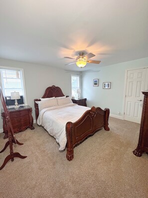 A bedroom with a wooden bed, a ceiling fan, a dresser, and a nightstand.