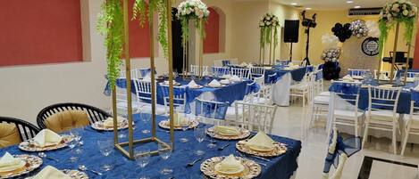 A banquet hall with tables set for a formal event, featuring blue tablecloths, white chairs, and floral centerpieces.