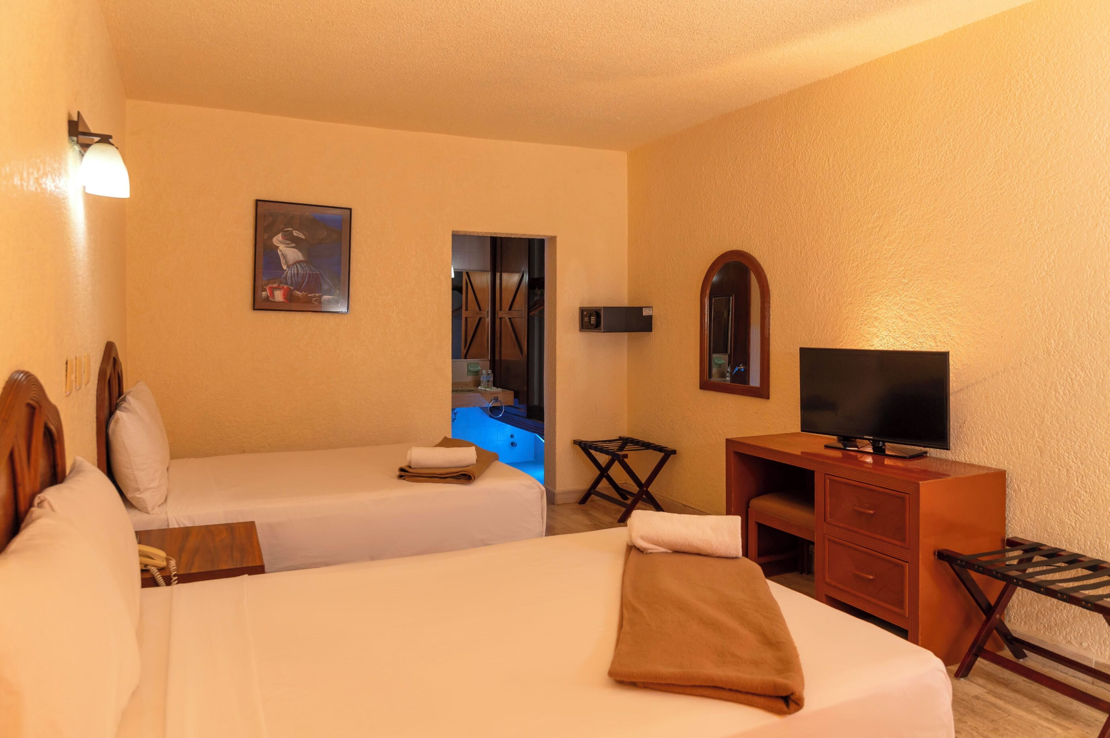 A hotel room with two beds, a desk, a television, and a bathroom with a bathtub.