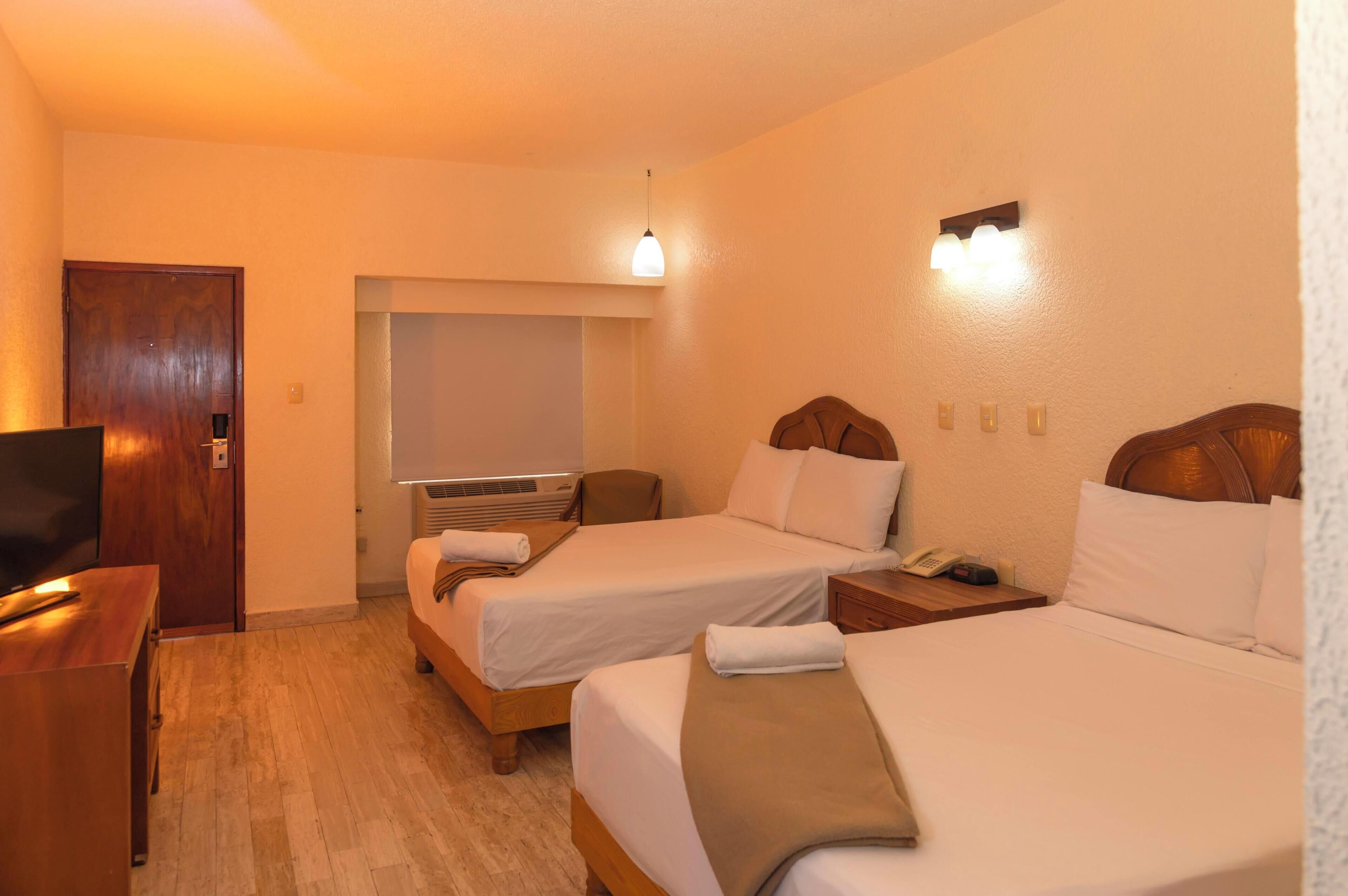A hotel room with two beds, a TV, a desk, and a window.