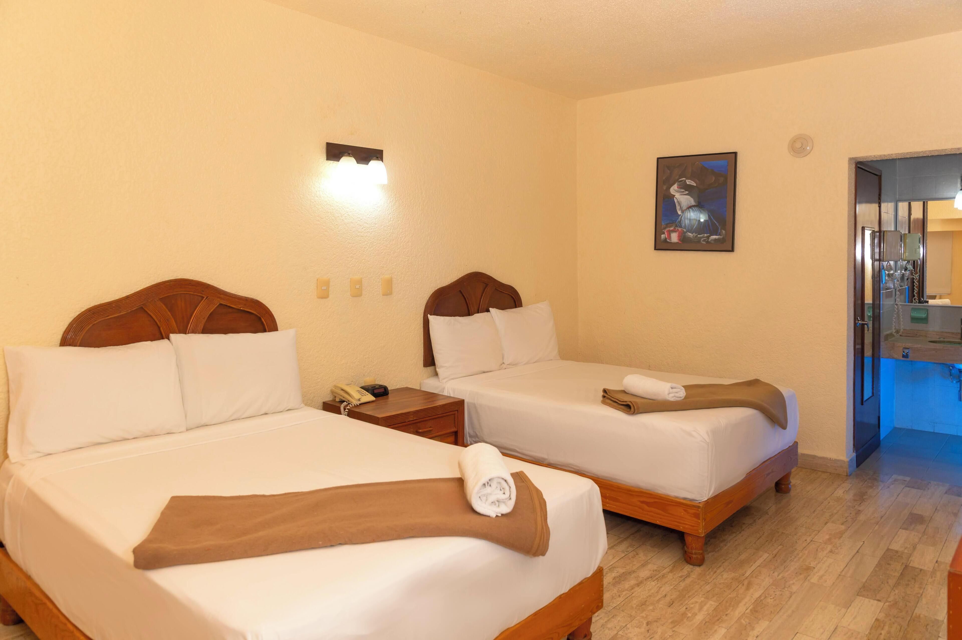 A hotel room with two beds, a nightstand, a painting, and a bathroom visible through an open door.
