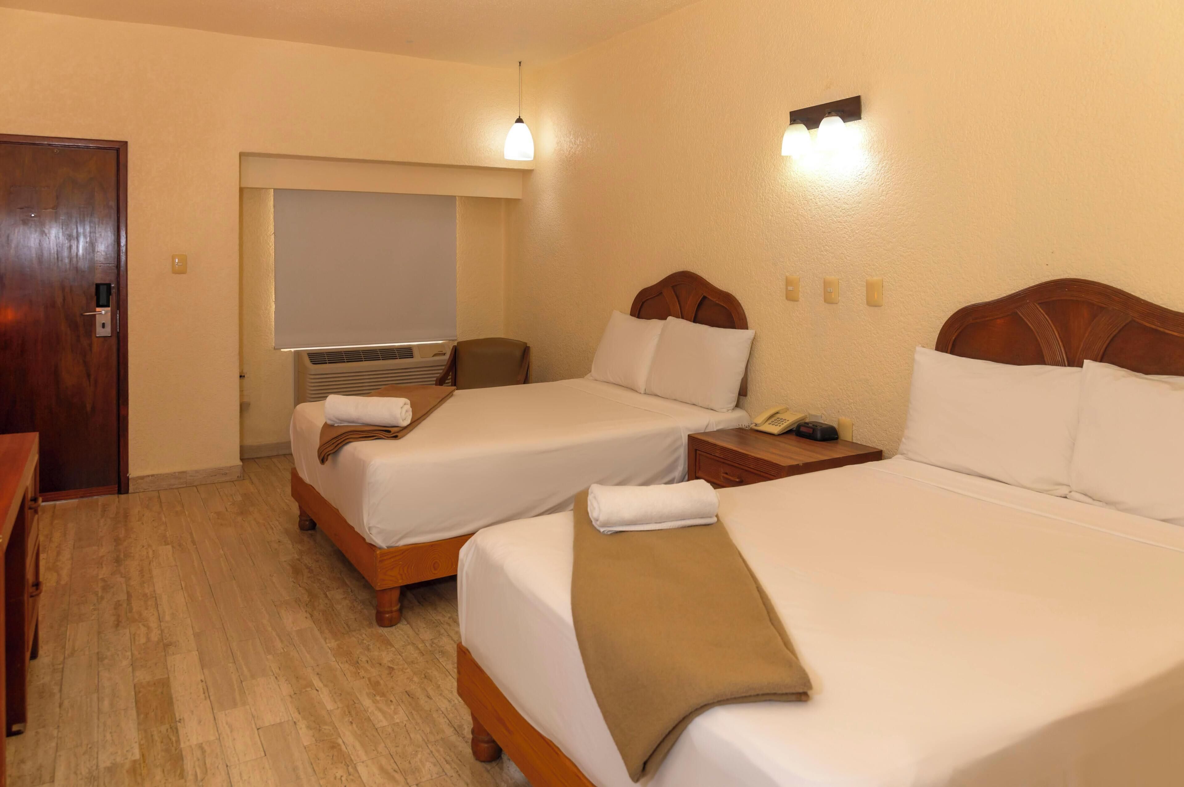 Habitación de hotel con dos camas, un escritorio, una silla, un televisor y un teléfono instalado en la pared.