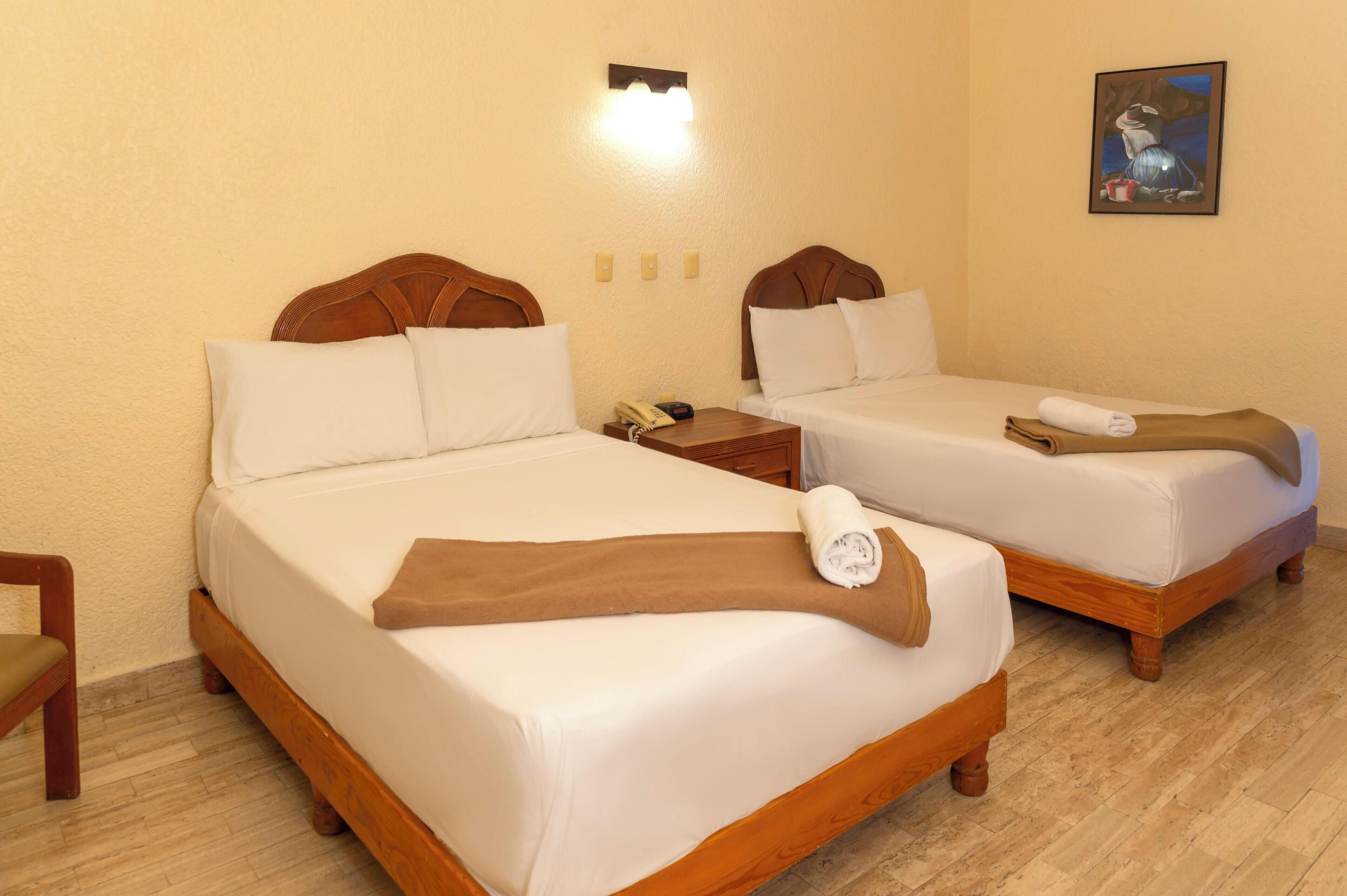 A hotel room with two beds, wooden headboards, white linens, a nightstand with a phone, a painting on the wall, and a wooden chair.