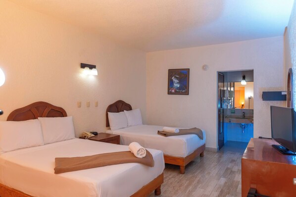 Une chambre d’hôtel avec deux lits, un bureau, une télévision et une salle de bain visible à travers une porte ouverte.