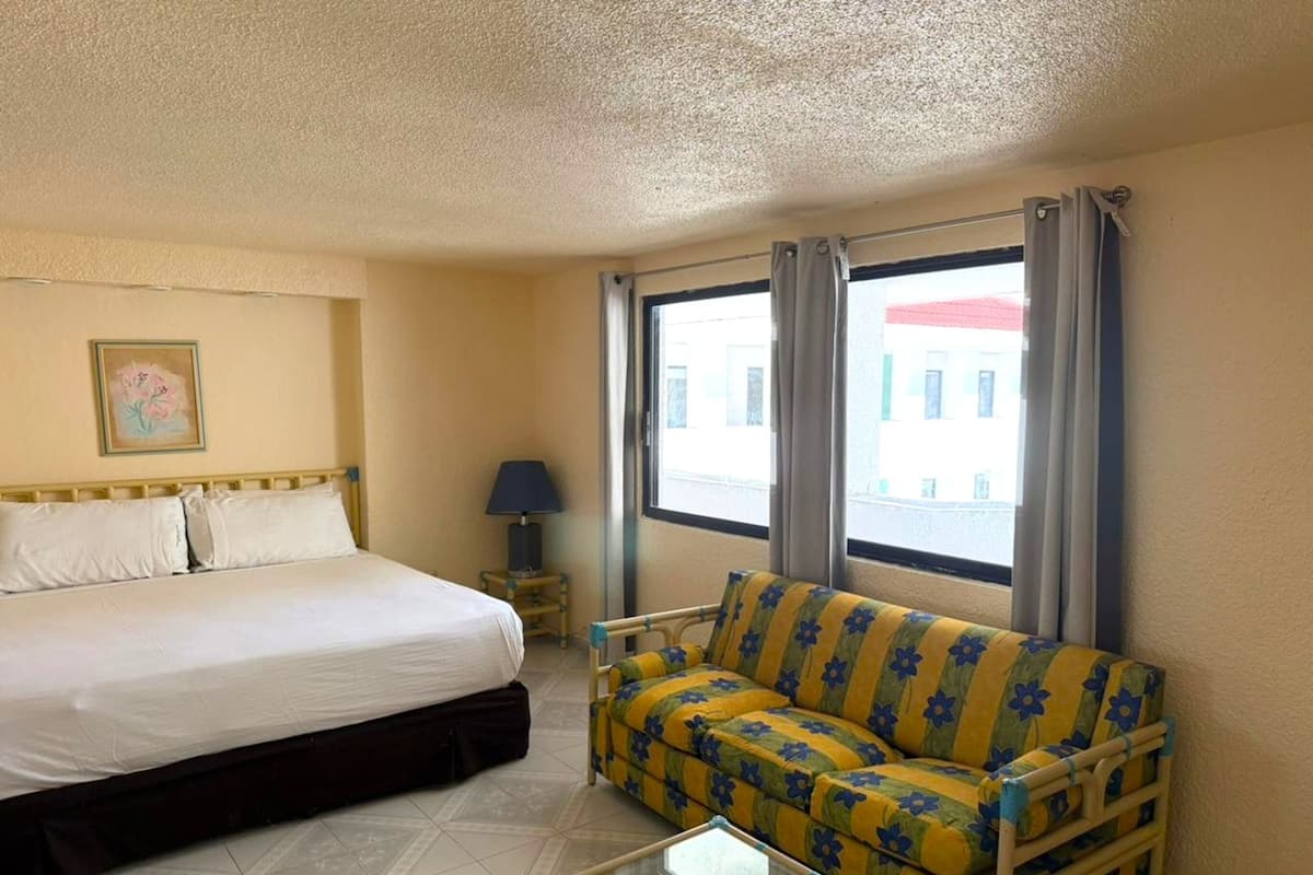 Una habitación de hotel con cama, sofá, una mesita y ventana con cortinas.