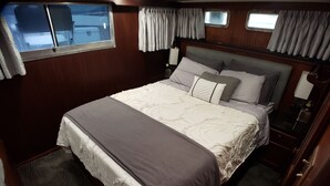 Un dormitorio con una cama grande, cortinas, un ventanal y una mesita de noche.