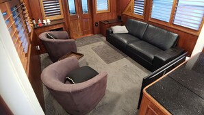 Un cuarto acogedor con un sofá de cuero negro, dos sillones morados, una puerta de madera con paneles de vidrio y una mesita con una lámpara.